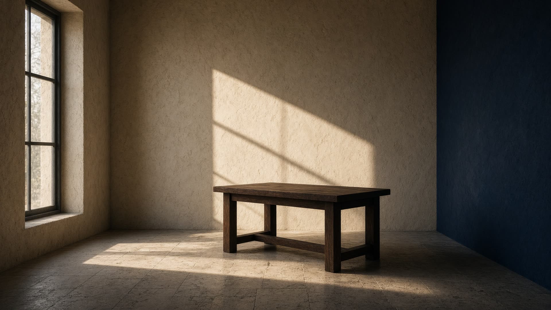A quiet limestone room with a single walnut table and late-afternoon light